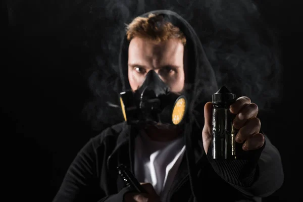 Человек в защитной маске фильтра курит электронную сигарету, показывая E-жидкость — стоковое фото
