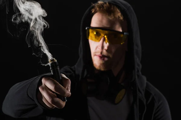 Hombre con gafas protectoras vapeo cigarrillo electrónico aislado en negro - foto de stock