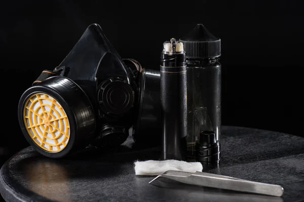Cigarrillo electrónico y mascarilla protectora aislada en negro - foto de stock