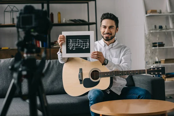 Sonriente bloguero de música mostrando notas y guitarra - foto de stock