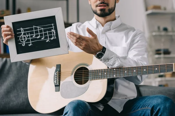 Cropped image of musician holding notes and guitar — Stock Photo