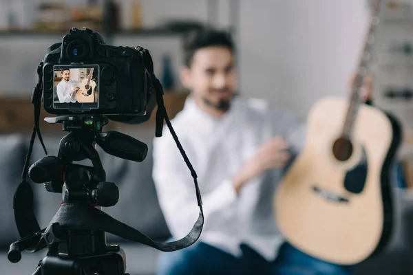 Music blogger holding and describing acoustic guitar with camera on foreground — Stock Photo