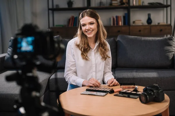 Blogueur beauté souriant assis à table avec des cosmétiques — Photo de stock