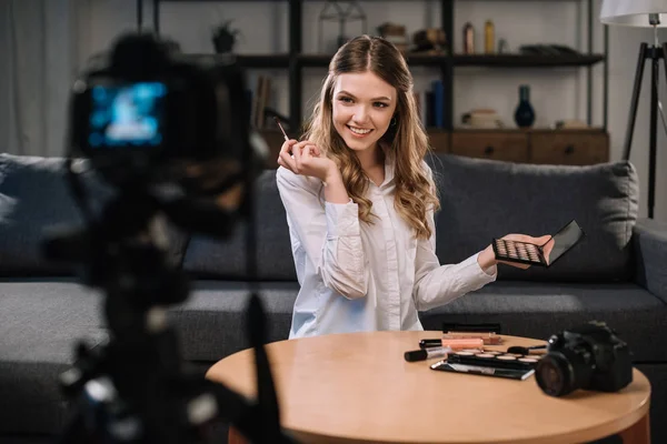 Sonriente belleza blogger con maquillaje cepillo y sombras de ojos - foto de stock