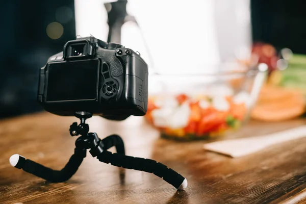 Macchina fotografica digitale sul tavolo con insalata su sfondo sfocato — Foto stock