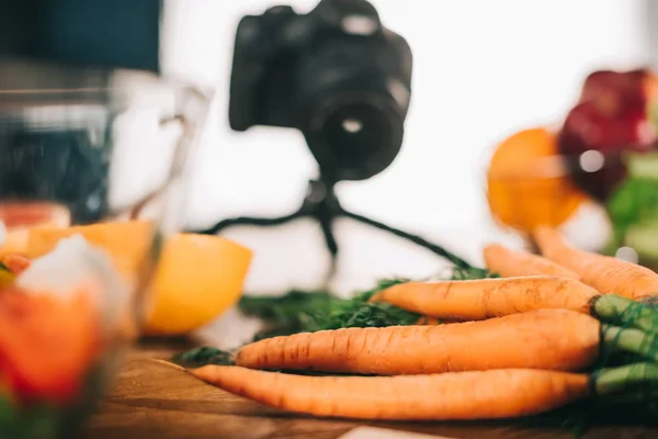 Carottes mûres sur table en bois avec caméra sur fond flou — Photo de stock