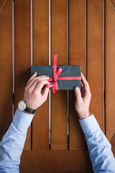 Imagen recortada del hombre atando cinta roja en la caja actual - foto de stock