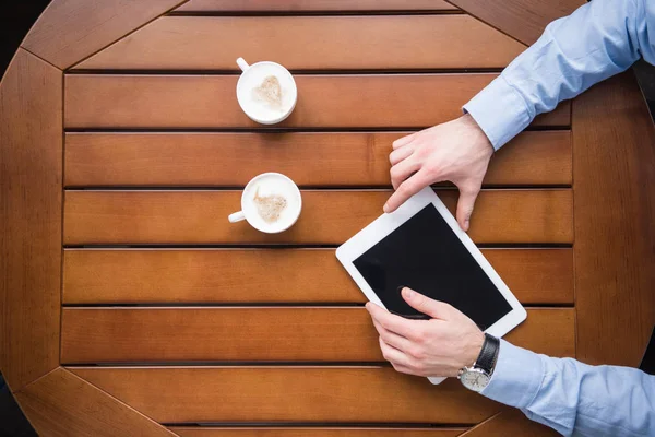 Cropped image of man holding tablet and sitting at table with two cups of coffee — Stock Photo