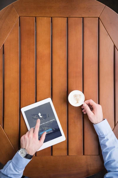 Cropped image of man sitting with coffee and loaded tumblr page on tablet — Stock Photo