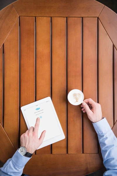 Imagem cortada do homem sentado com café e carregado skype página no tablet — Fotografia de Stock