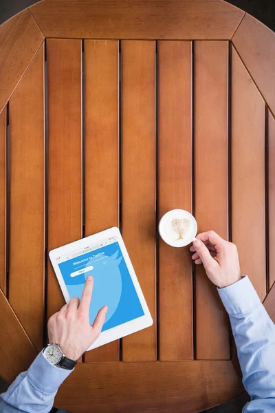 Cropped image of man sitting with coffee and loaded twitter page on tablet — Stock Photo