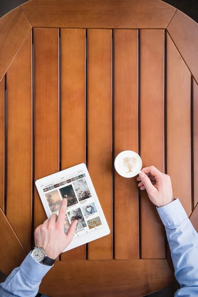 Immagine ritagliata di uomo seduto con caffè e caricato pagina pinterest su tablet — Foto stock