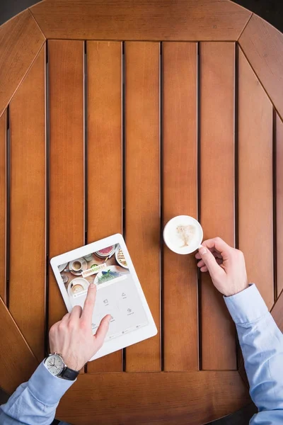 Cropped image of man sitting with coffee and loaded foursquare page on tablet — Stock Photo