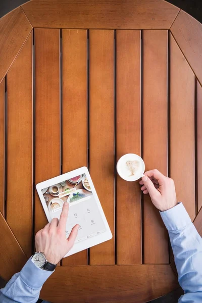 Imagem cortada do homem sentado com café e carregado página quadrangular no tablet — Fotografia de Stock