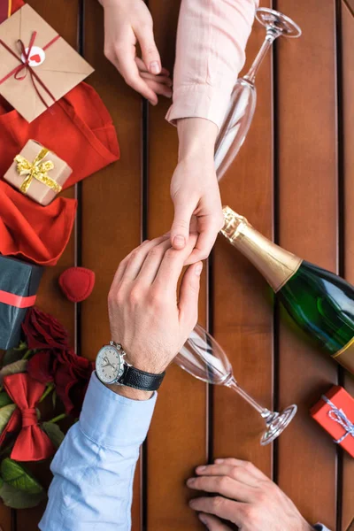 Imagen recortada de pareja cogida de la mano en la mesa con regalos - foto de stock