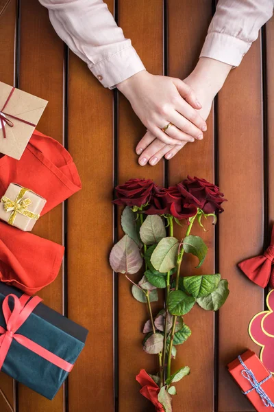 Imagen recortada de la mujer sentada con ramo de rosas y regalos en la mesa - foto de stock
