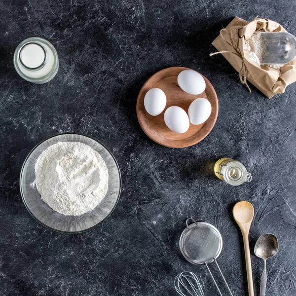 Vista superior de utensílios de cozinha dispostos e ingredientes para panificação na superfície de mármore escuro — Fotografia de Stock