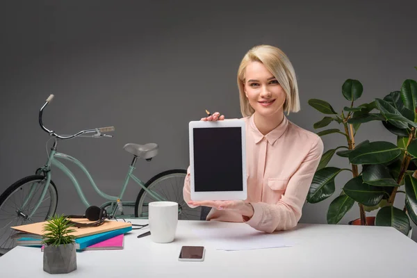 Retrato de una mujer de negocios sonriente mostrando tableta en el lugar de trabajo aislada en gris - foto de stock