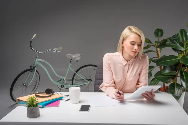 Красива молода бізнес-леді, використовуючи планшет на робочому місці ізольована на сірому — стокове фото