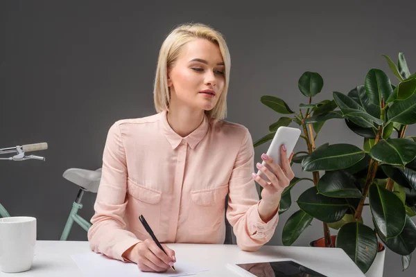 Portrait de jeune femme d'affaires utilisant un smartphone sur le lieu de travail isolé sur gris — Photo de stock