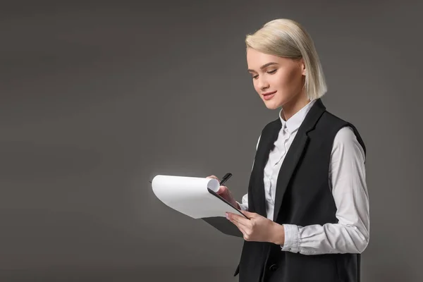 Porträt einer stilvollen Geschäftsfrau, die Notizen im Notizblock macht, isoliert auf grau — Stockfoto