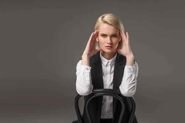 Портрет молодой стильной женщины, сидящей на стуле и смотрящей на камеру, изолированную на сером — стоковое фото