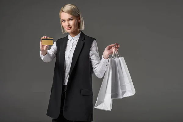 Retrato de mujer elegante con tarjeta de crédito y bolsas de compras aisladas en gris - foto de stock