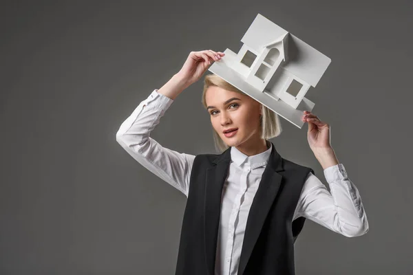 Portrait of young real estate agent with house model isolated on grey — Stock Photo