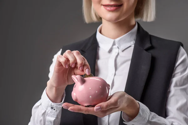 Cropped shot of businesswoman putting coin into piggy bank isolated on grey — Stock Photo