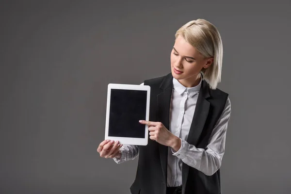 Retrato de una hermosa joven apuntando a una tableta con pantalla en blanco aislada en gris - foto de stock