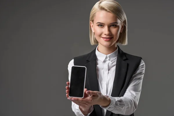 Porträt einer lächelnden Frau zeigt Smartphone mit leerem Bildschirm isoliert auf grau — Stockfoto