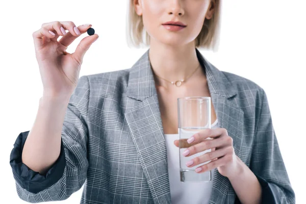 Vista recortada de una mujer sosteniendo un vaso de agua y un comprimido de carbón activado, aislado en blanco - foto de stock