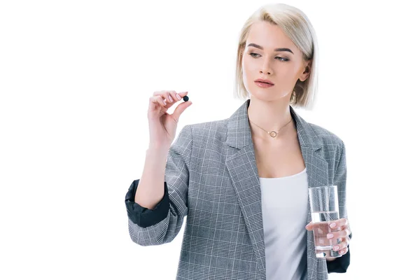 Женщина держит стакан воды и активированный уголь таблетки, изолированные на белом — стоковое фото