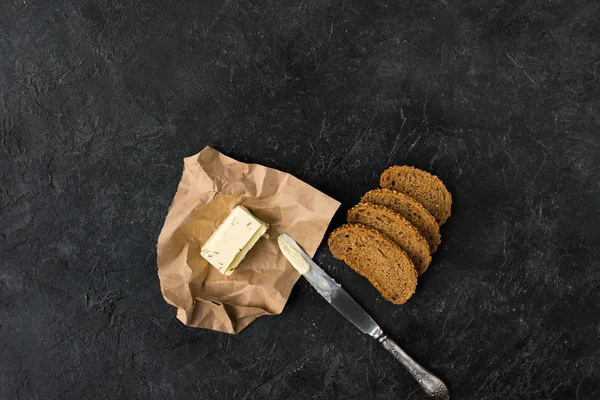 Draufsicht auf Brotscheiben, Butterrand-Messer auf dunkler Tischplatte — Stockfoto