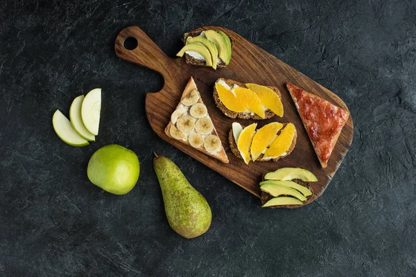 Flat lay with snacks for healthy breakfast with fruits on wooden cutting board on dark tabletop — Stock Photo