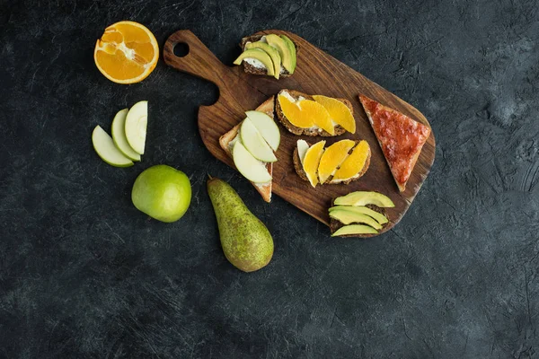 Плоская лежала с закусками для здорового завтрака с фруктами на деревянной разделочной доске на темной столешнице — стоковое фото