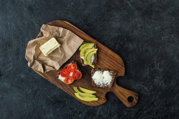 Flat lay with snacks for healthy breakfast on wooden cutting board on dark tabletop — Stock Photo