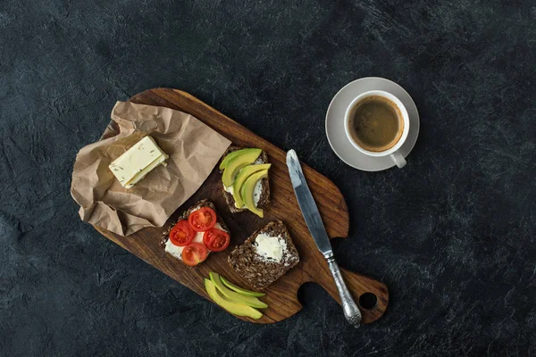 Flat lay with snacks for healthy breakfast and cup of coffee on wooden cutting board on dark tabletop — Stock Photo