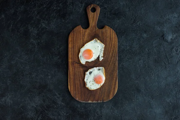 Vista superior de huevos fritos en tabla de cortar de madera en la superficie oscura - foto de stock