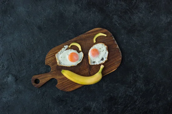 Vista superior de la cara sonriente hecha de comida para un desayuno saludable en la tabla de cortar - foto de stock