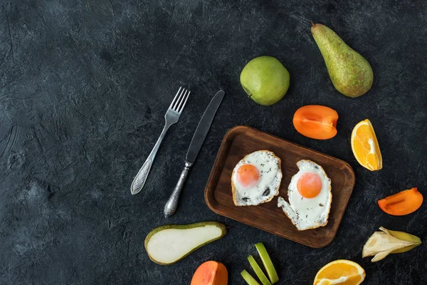 Flat lay with healthy breakfast with fried eggs and fruits on dark tabletop — Stock Photo