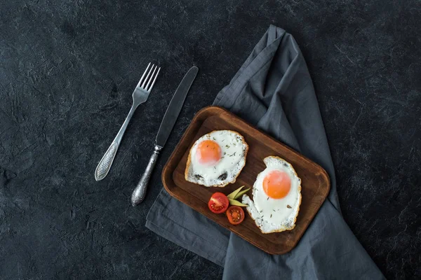 Вид зверху смажені яйця зі скибочками вишневих помідорів на сніданок на темній стільниці — стокове фото