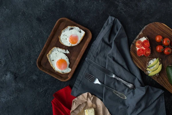 Vista superior de los huevos fritos y sabrosos bocadillos saludables para el desayuno en la mesa oscura - foto de stock