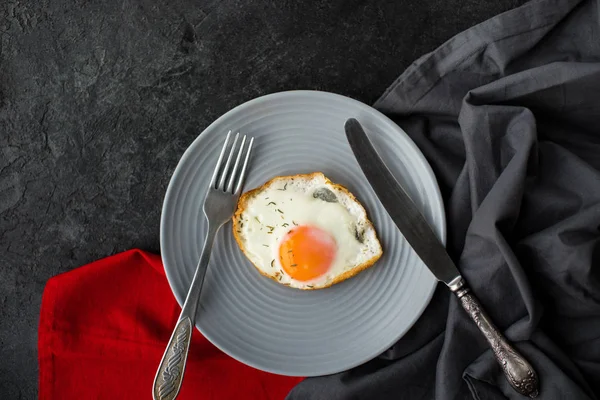 Vue de dessus de l'oeuf frit sur assiette pour le petit déjeuner avec couverts sur la surface sombre — Photo de stock