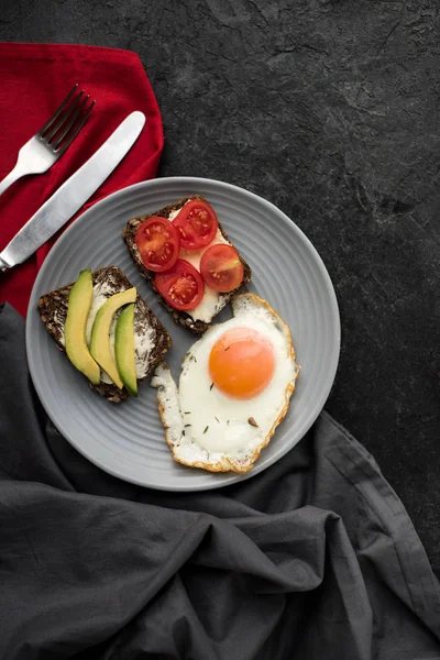 Vista superior del huevo frito y aperitivos para el desayuno en el plato en la mesa oscura - foto de stock