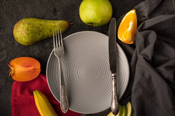 Blick auf den leeren Teller mit Besteck und frischem Obst auf der Tischplatte — Stockfoto