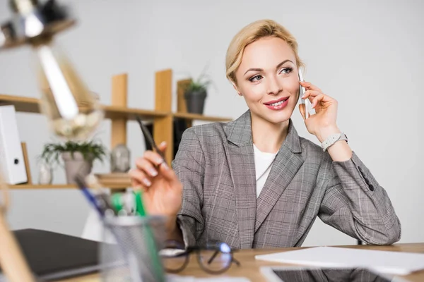 Retrato de la alegre mujer de negocios hablando en el teléfono inteligente en el lugar de trabajo - foto de stock