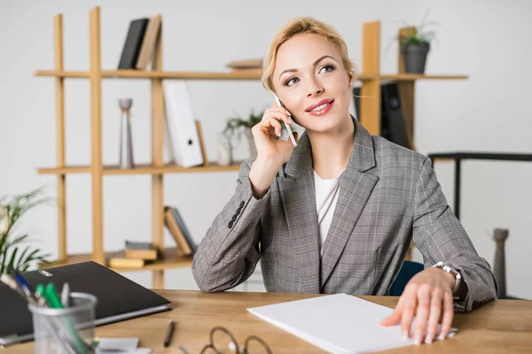 Smiling businesswoman talking on smartphone at workplace in office — Stock Photo