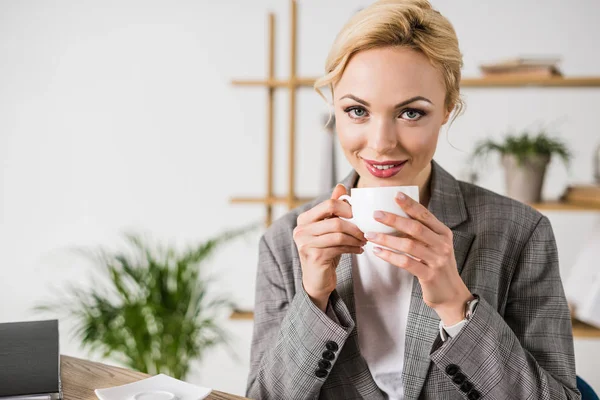 Портрет веселой красивой деловой женщины с чашкой кофе, смотрящей в камеру — стоковое фото