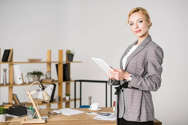 Retrato de empresaria confiada con tableta de pie en el lugar de trabajo en la oficina - foto de stock